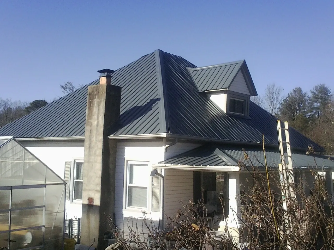 Dark blue standing seam metal roof on a white farmhouse with dormer — Slate & Tile Roof Repair by Roofing Brothers in Rapids City