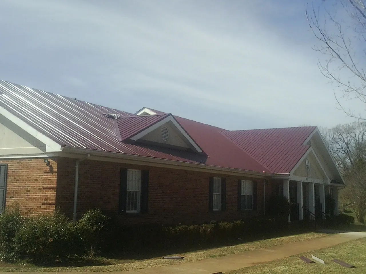 Red metal roof with gabled entries on a long brick building, from a Hail Damage Roof Repair job in Rapids City