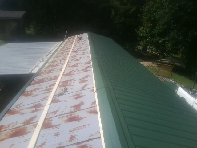 Old rusted panels beside newly installed green metal roofing — Wind Damage Roof Repair by Roofing Brothers in Rapids City