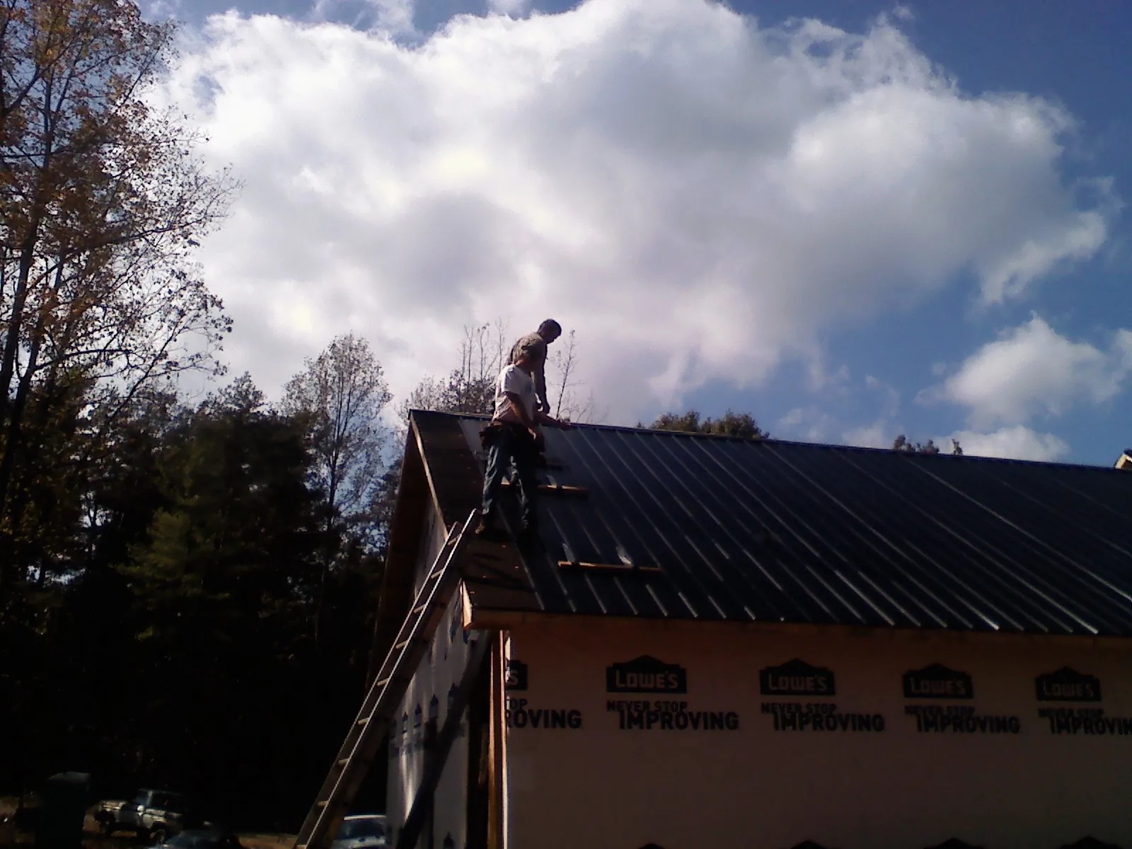 Roofer fastening dark metal panels high against a cloudy sky, from a Roof Inspection job in Rapids City